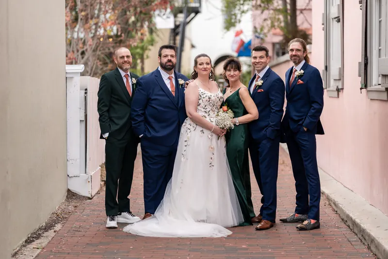 The full wedding party standing together in a narrow brick alley with pink-walled buildings in downtown St. Augustine