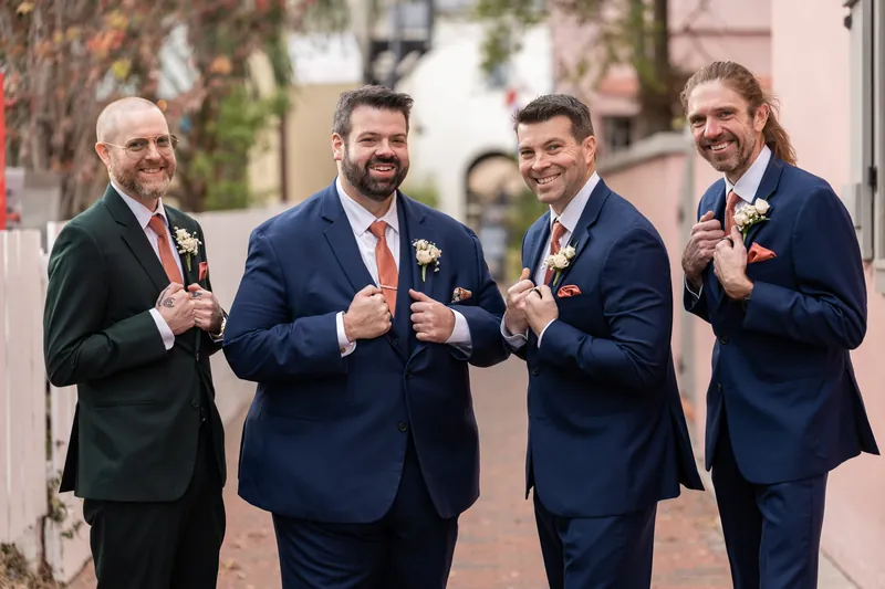The groom and his three groomsmen adjusting their jackets and showing off their boutonnieres in a downtown alley