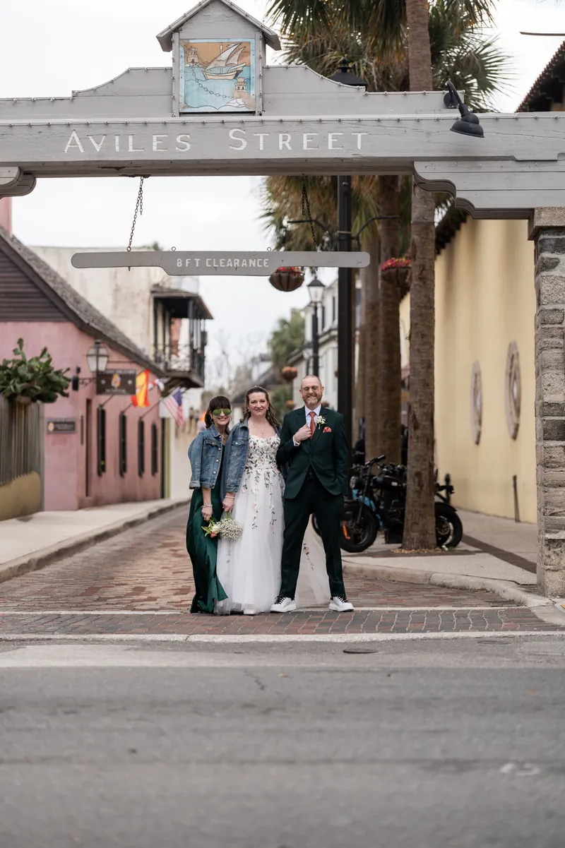 The bride walking under the Aviles Street sign with her maid of honor and best man on either side