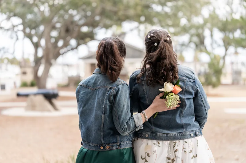 The bride and her maid of honor seen from behind, arms around each other, wearing matching denim jackets in the Plaza