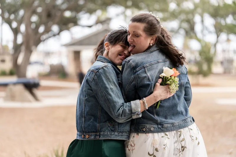 The bride and maid of honor hugging and laughing together, both in matching denim jackets at the Plaza