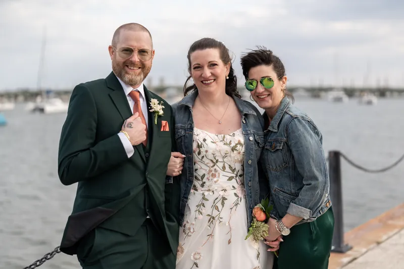 The bride posing on the bayfront dock with her best man and maid of honor, sailboats and the bay behind them