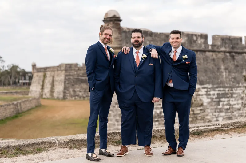 The groom and his groomsmen standing in front of the Castillo de San Marcos, arms around each other