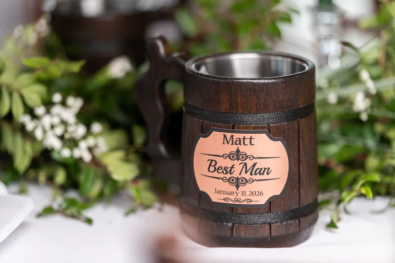 A personalized wooden Best Man mug engraved with Matt and the wedding date, nestled among greenery on the reception table