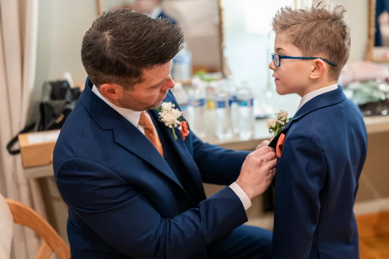 A groomsman pinning a boutonniere on a young ring bearer in a matching navy suit before the ceremony
