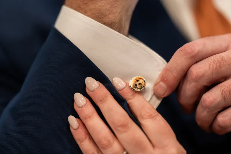 Close-up of the bride's hand resting on the groom's sleeve, showing a custom cufflink with a photo of their dog
