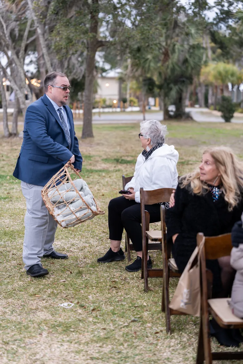 A man carrying a basket of blankets to hand out to guests seated for the outdoor winter ceremony