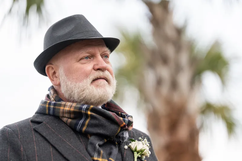 The officiant in a gray hat, plaid scarf, and pinstripe jacket waiting for the ceremony to begin