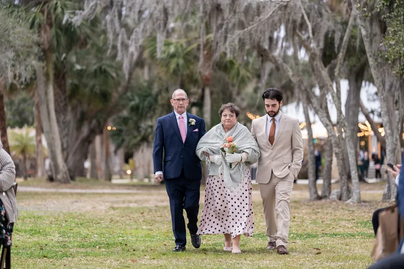 The groom's grandmother escorted down the aisle by two family members under Spanish moss and string lights