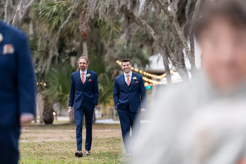 Two groomsmen walking down the aisle together under Spanish moss with string lights behind them