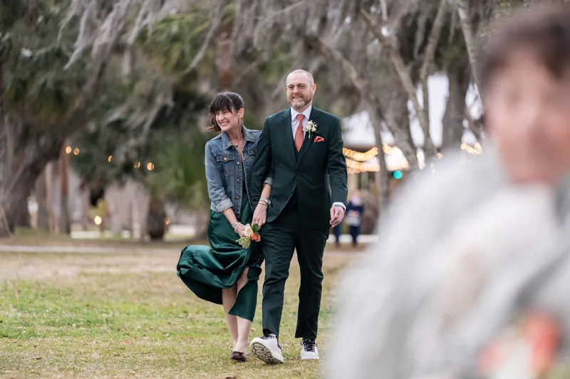 The maid of honor and best man walking arm-in-arm down the aisle, smiling, with the bride visible in the foreground