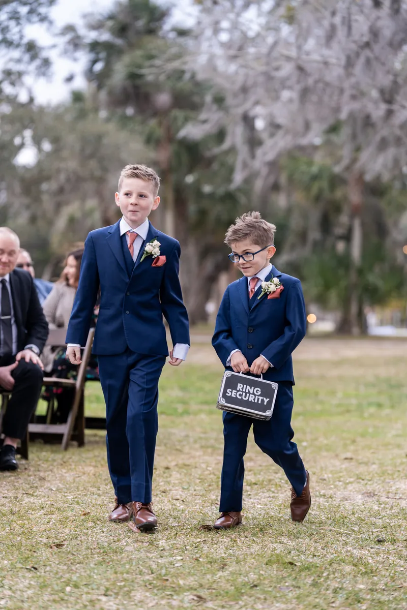 Two ring bearers in navy suits walking down the aisle together, one carrying a Ring Security briefcase