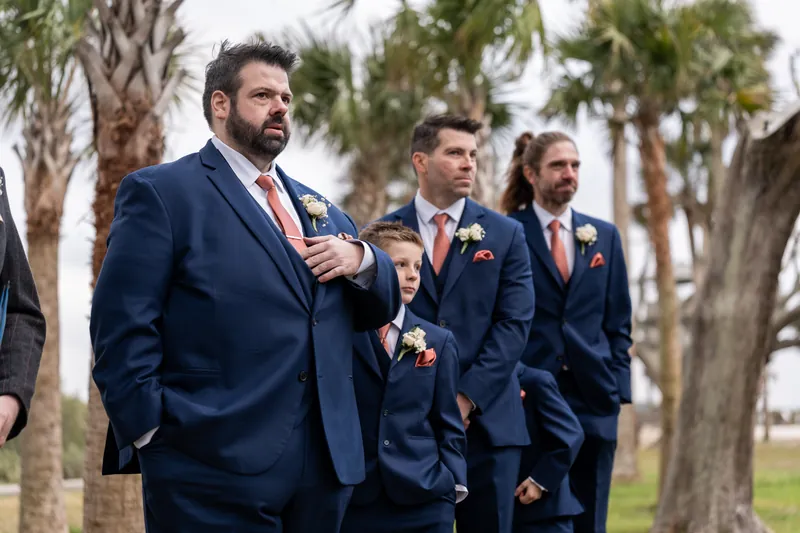 Chase standing at the altar with his groomsmen and ring bearer, watching the bride approach beneath palm trees