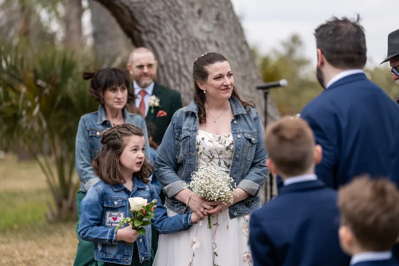 Anne holding hands with her daughter Mara at the altar as the ceremony begins, the maid of honor looking on behind them
