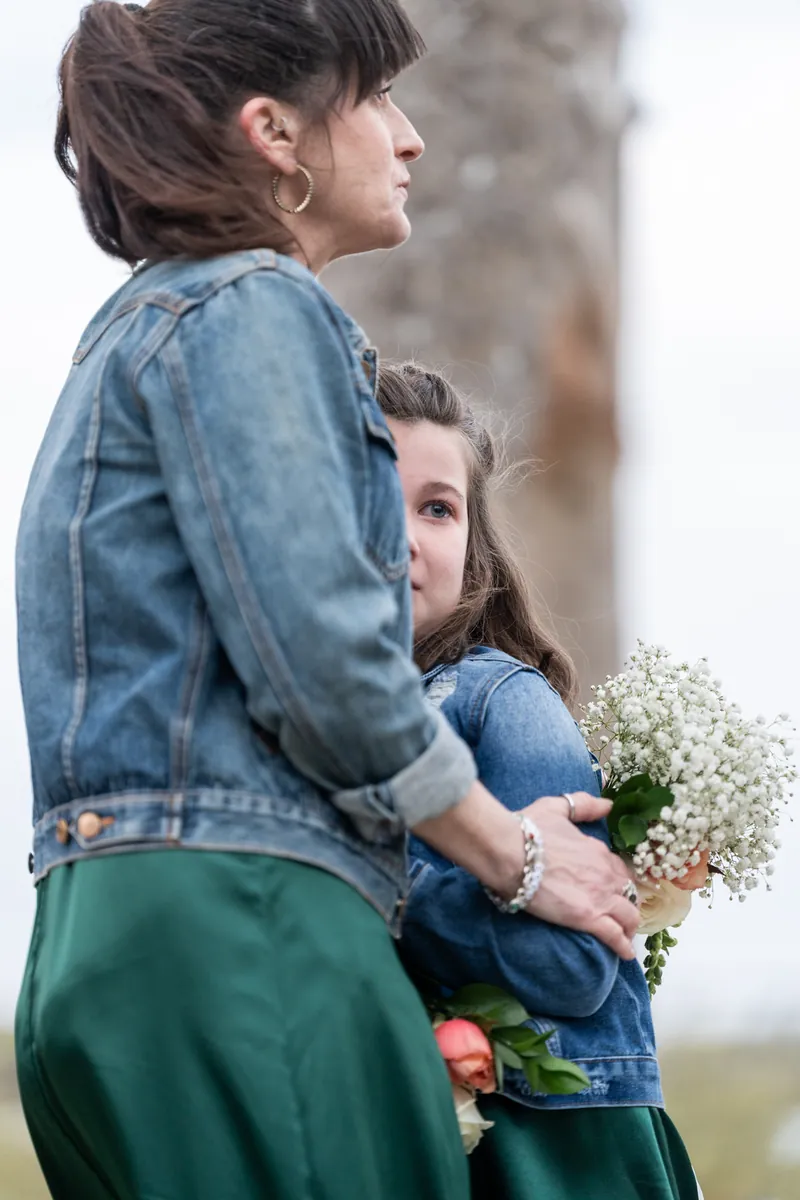 The maid of honor holding a flower girl close while watching the ceremony, baby's breath and colorful flowers between them