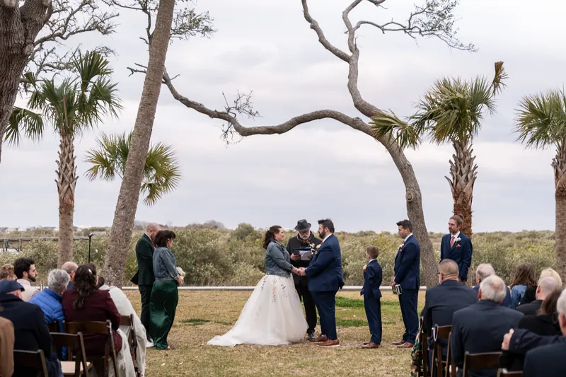 Wide view of the ceremony beneath twisting palms at Fountain of Youth, the wedding party and seated guests framed by dramatic clouds