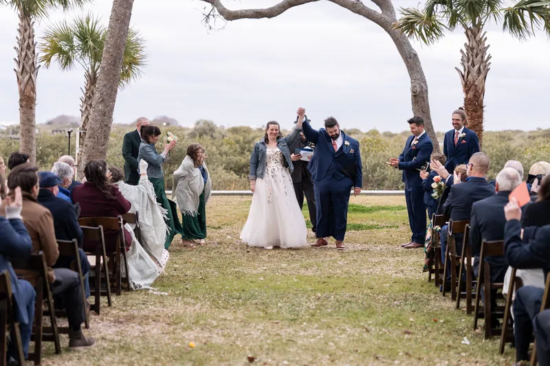 The newlyweds raising their joined hands and walking back down the aisle together as guests cheer