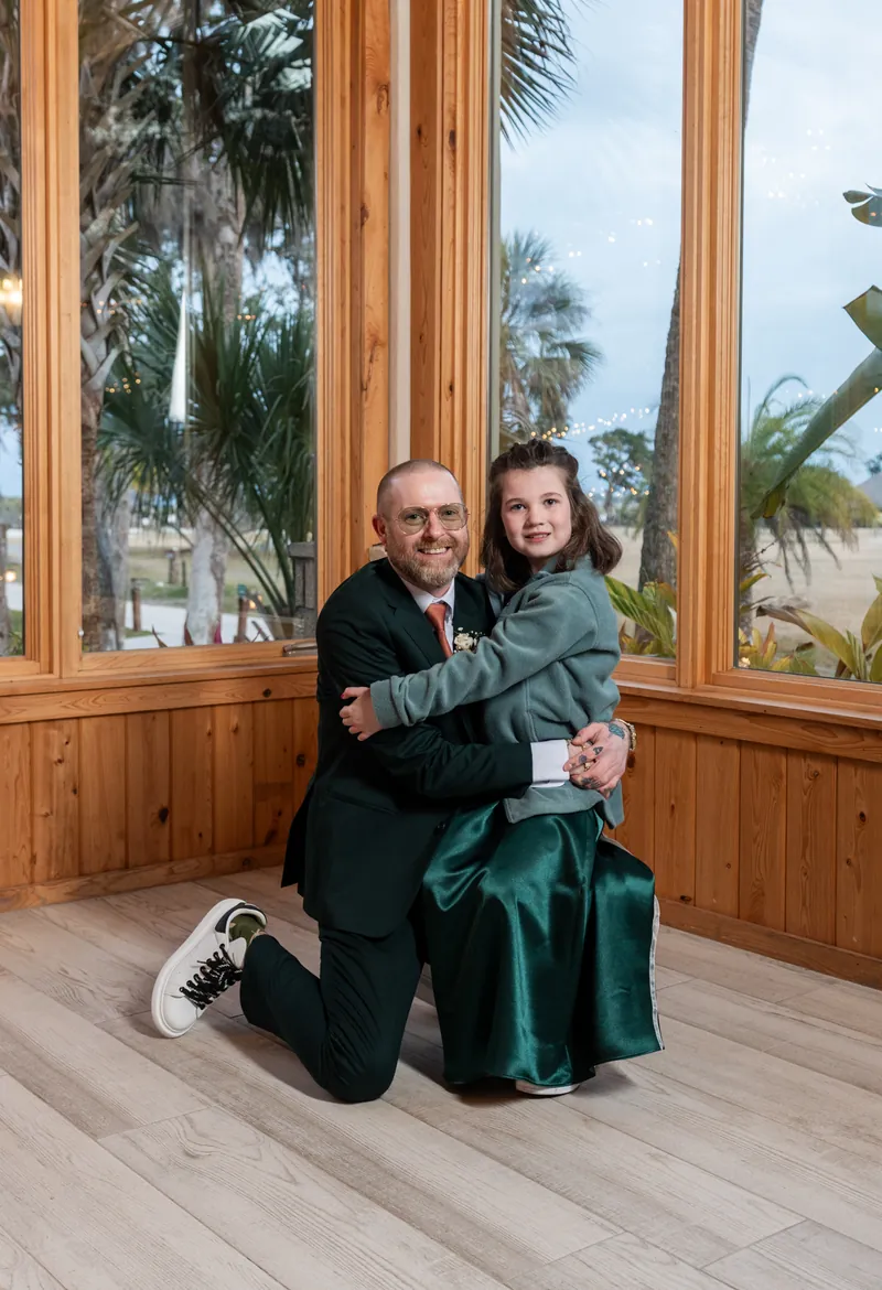 The best man kneeling and hugging one of the flower girls in the Fountain of Youth reception pavilion