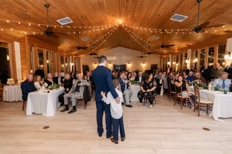 The groom speaking to guests during the reception in the Fountain of Youth pavilion, string lights overhead and guests at round tables