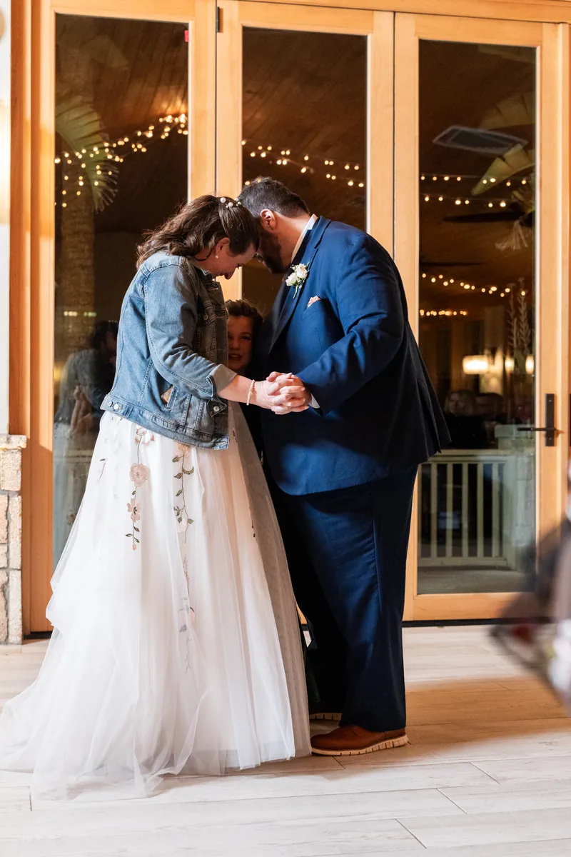 The couple and a child sharing a tender moment during the first dance, foreheads close together in front of the glass doors