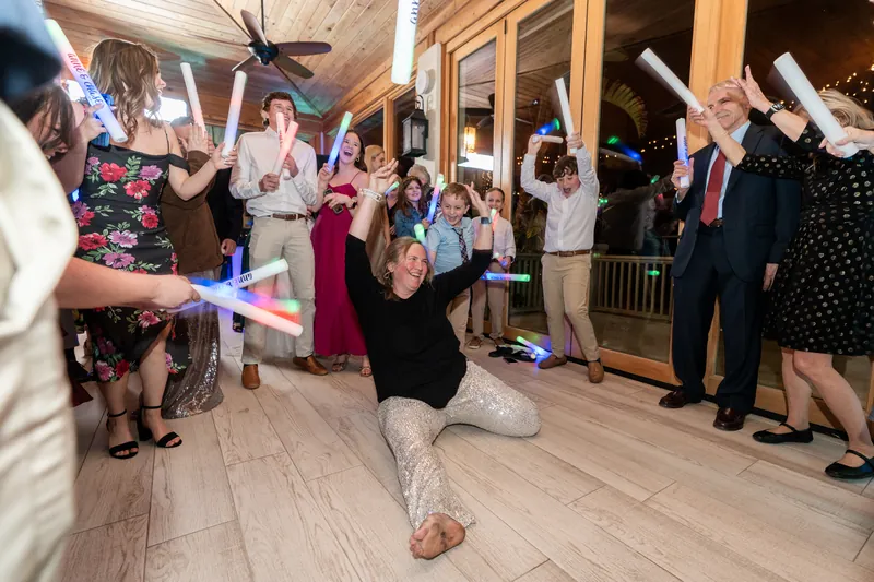 A wedding guest doing the splits on the dance floor while the crowd waves LED glow sticks and cheers her on