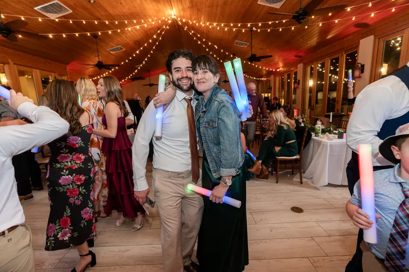 The bridesmaid posing with a young man on the dance floor, both holding glow sticks under the string lights