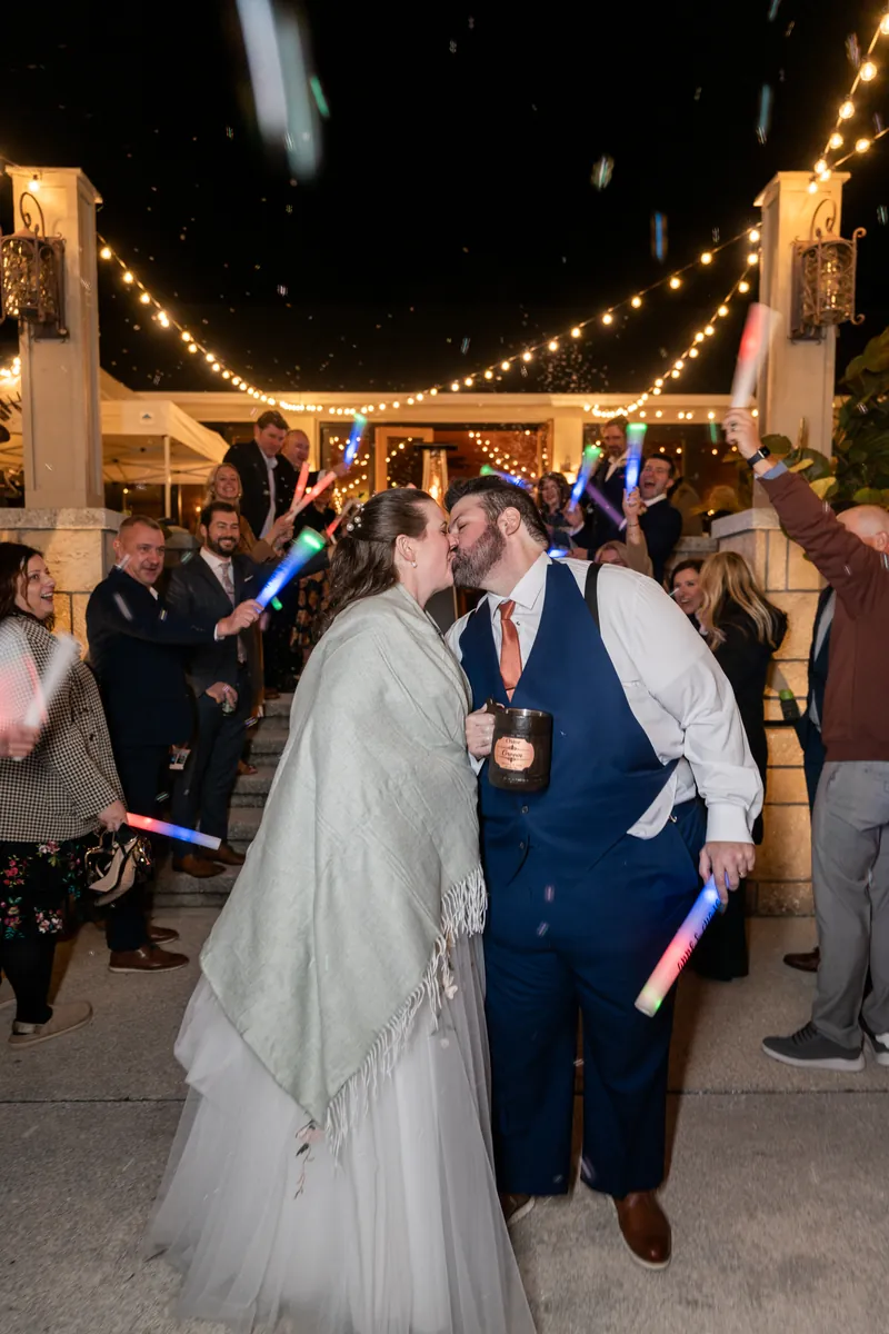 The newlyweds sharing a kiss during their grand exit as guests wave glow sticks and confetti falls under the Fountain of Youth string lights