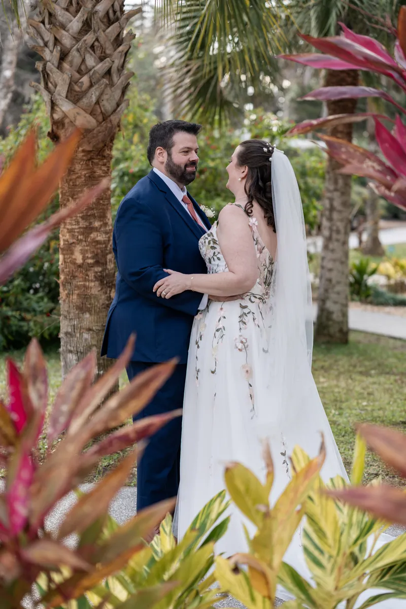 Anne and Chase stand by palm fronds at the St. Augustine Bayfront in formal wedding attire.
