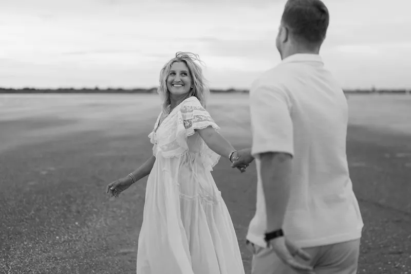 Black and white portrait of Ashley looking over her shoulder at Craig as they stand together on the expansive beach.