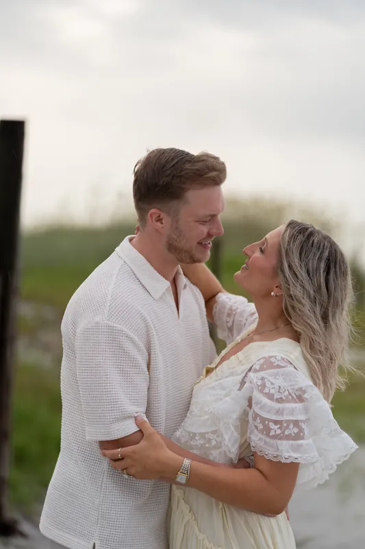 Ashley and Craig embrace near dune grasses, foreheads nearly touching as they smile at each other during golden hour.