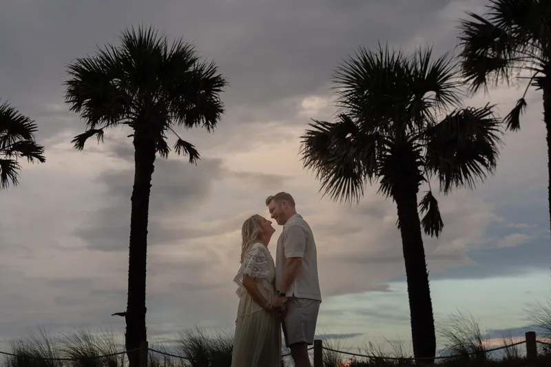 Framed by palm trees at dusk, Ashley and Craig stand close together beneath a darkening sky at Vilano Beach.