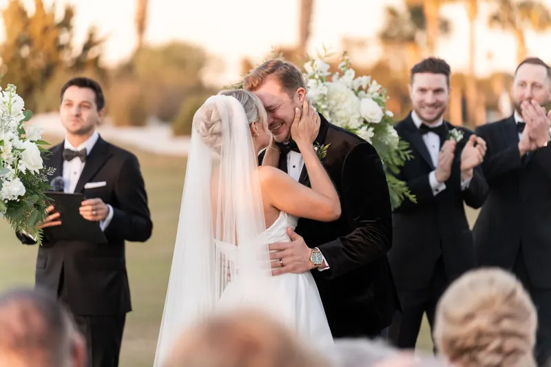 Craig and Ashley embrace during the ceremony as groomsmen holding bouquets watch from the sidelines.