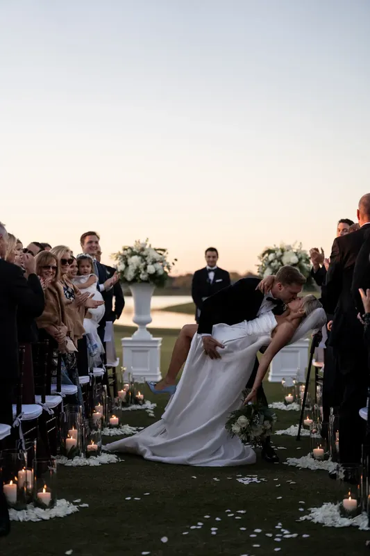 Ashley's train trails behind her as she walks down the aisle lined with candles and guests during the outdoor ceremony.