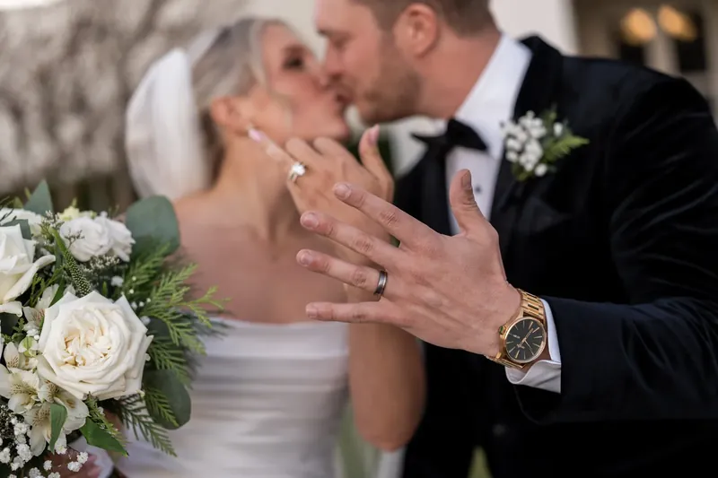 Ashley and Craig kiss while holding their wedding bouquet and boutonniere.