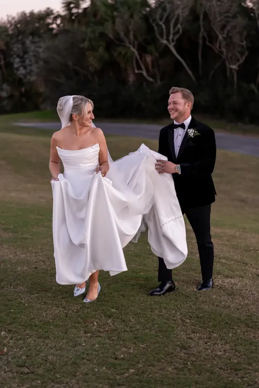 Craig walks beside Ashley across the lawn as her white gown trails behind them.
