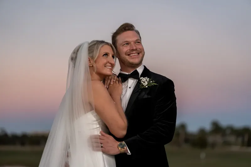 Ashley leans against Craig's shoulder at twilight in her veil and white dress.