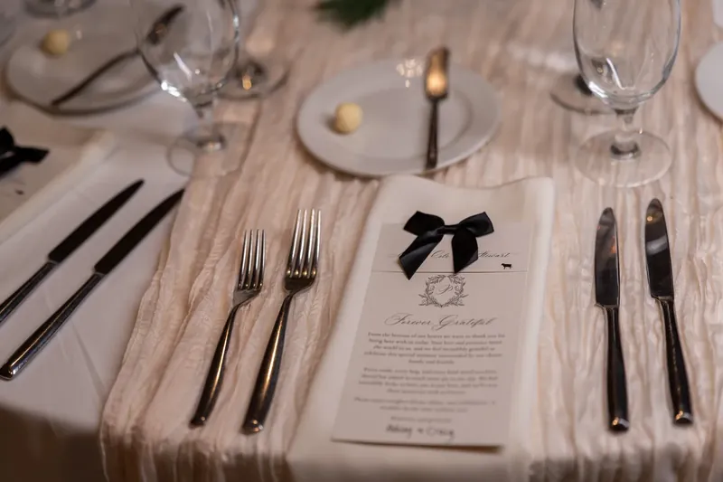Black flatware and a napkin with bow accent a cream place setting at the reception table.