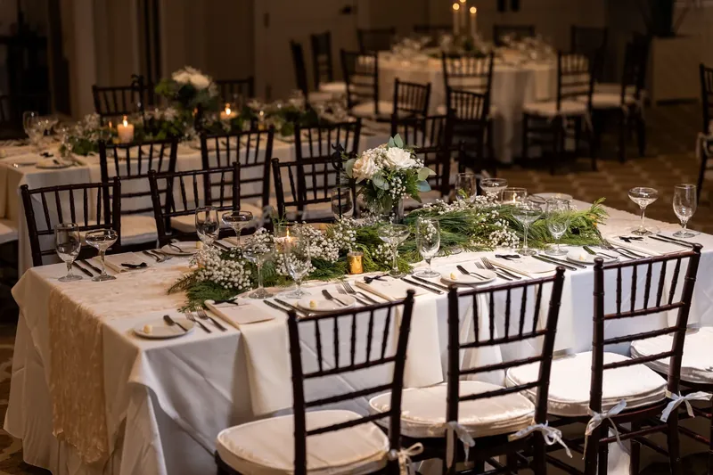 Cream linens and black chiavari chairs frame green-and-white floral centerpieces in the ballroom.
