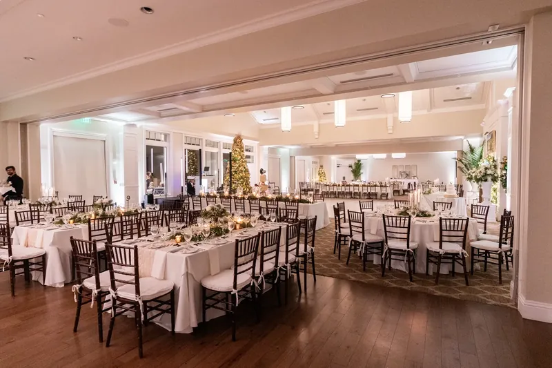 Round tables with cream linens and dark chiavari chairs fill a bright ballroom with floral centerpieces.