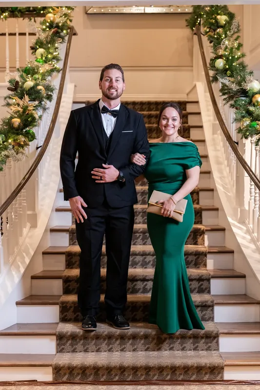 Craig in a dark suit and Ashley in an emerald gown descend a staircase framed by garland.