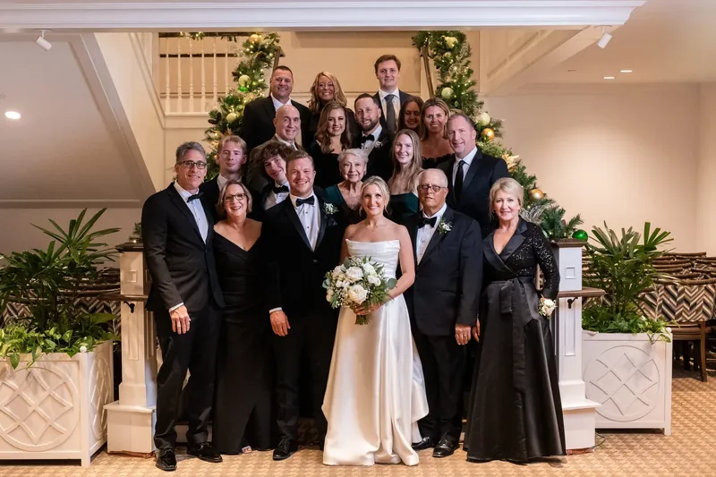 Ashley in a white gown and wedding party of thirteen pose on a staircase landing.
