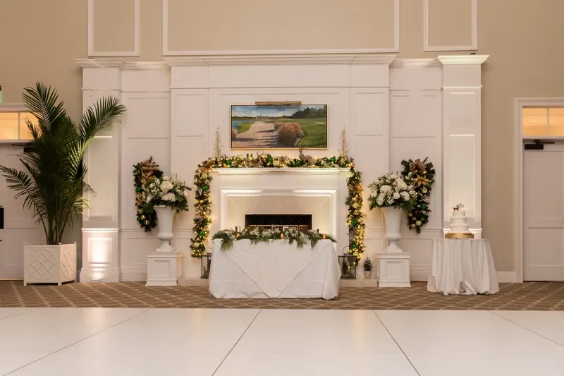A fireplace mantel decorated with garland and flanking topiaries serves as the backdrop for a gift table at the reception.