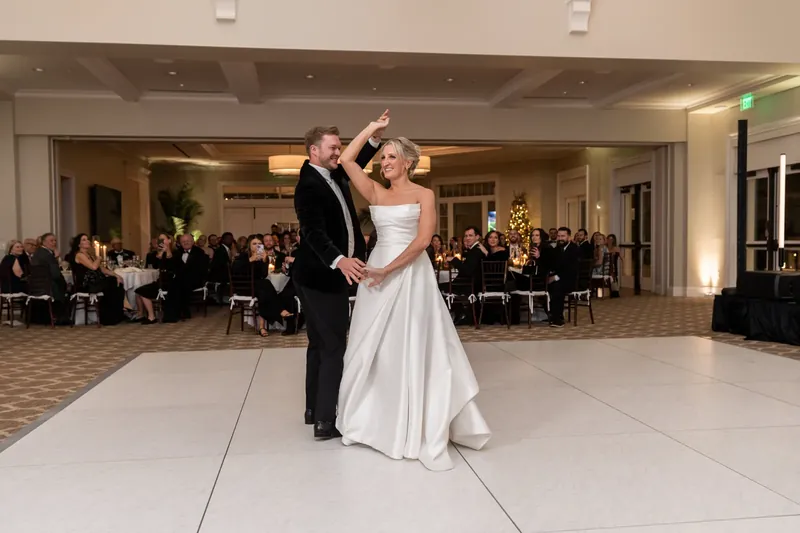 Ashley and Craig smile during their first dance with guests seated around them.