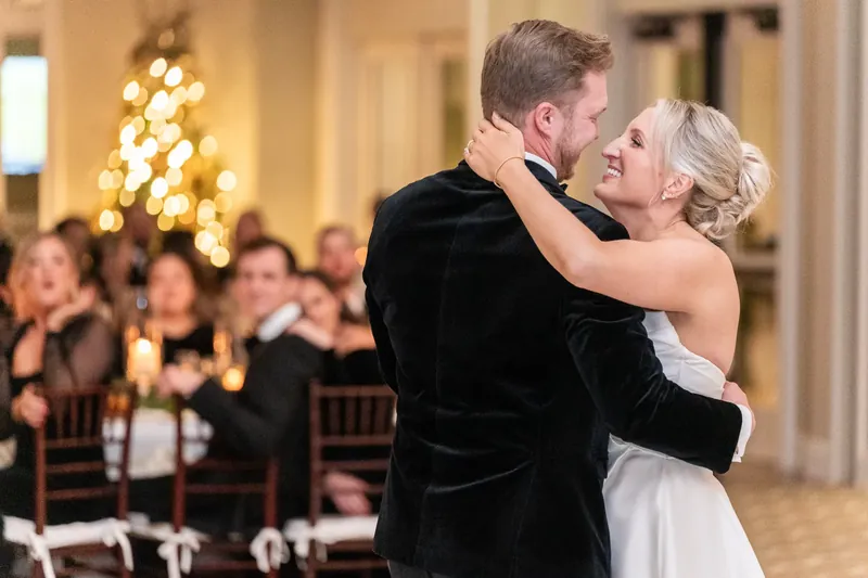 An older woman dances with Craig, smiling warmly while guests seated behind them applaud.