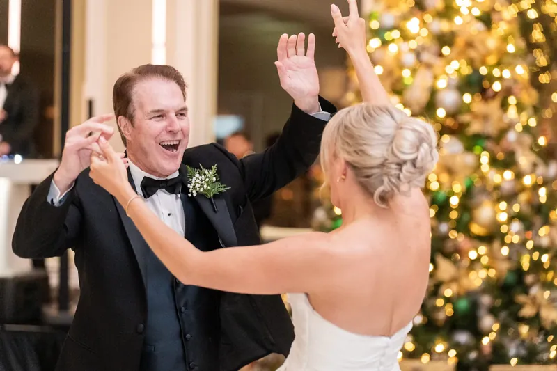 Craig and Ashley dance with arms raised, a lit Christmas tree glowing behind them.