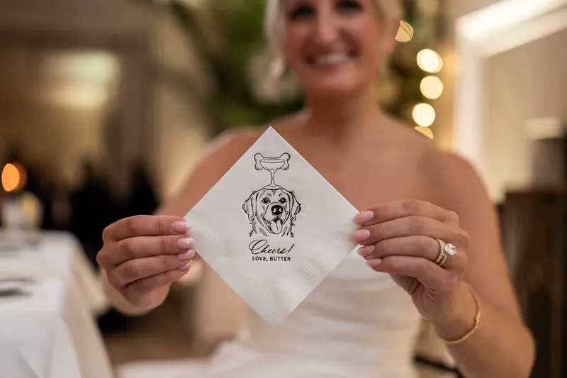 Ashley holds up a personalized napkin printed with their names and a dog illustration.