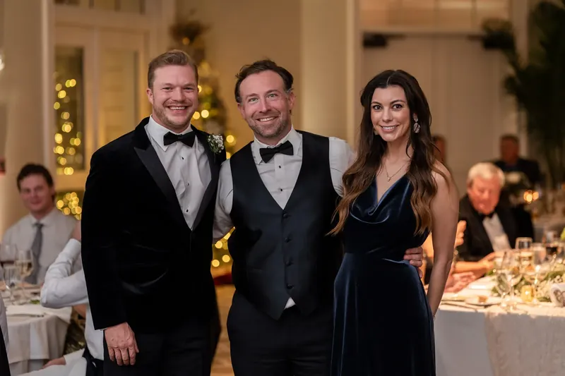 Craig stands between two guests in formal attire at the reception.