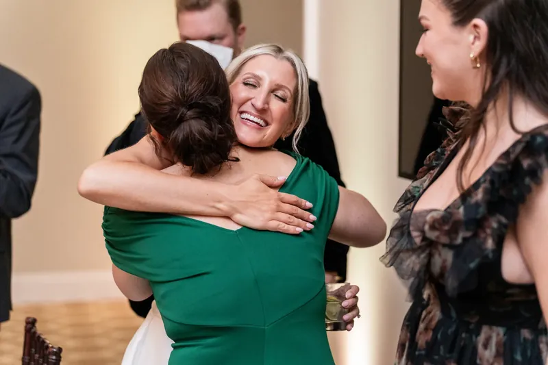 A woman in green hugs a guest while another watches nearby at the reception.