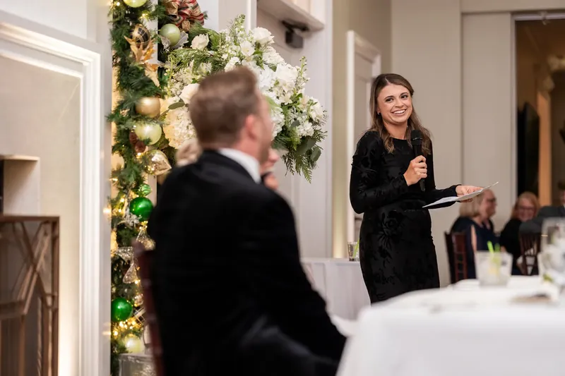 A woman in black gives remarks to guests gathered for the reception.