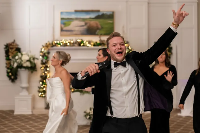Craig throws one arm skyward while dancing, with Ashley and other guests celebrating around him on the ballroom floor.